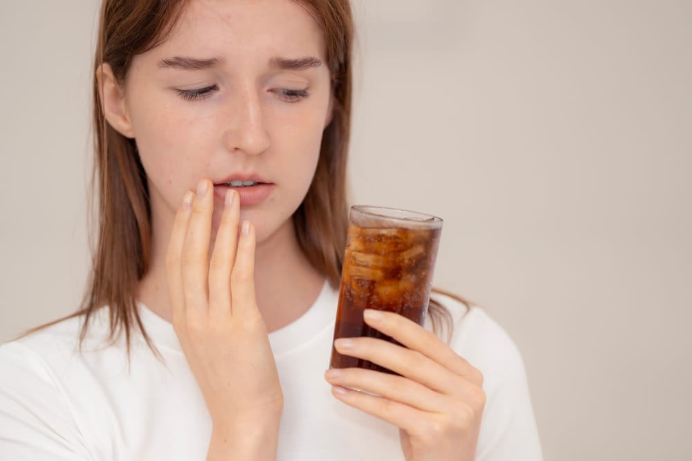Young woman with toothache holding a glass of cold soda, showing discomfort and dental sensitivity