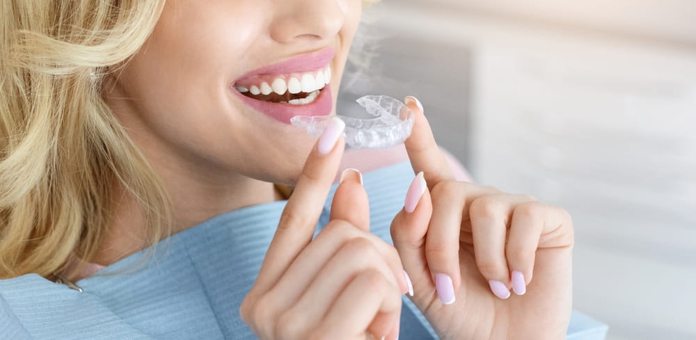 Unrecognizable blonde woman with healthy white teeth holding invisible braces