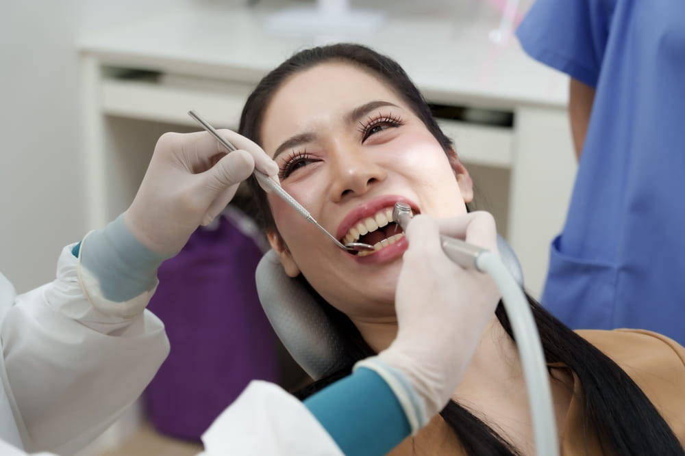 dentist using dental mirror and scaler examining mouth of asian adult female