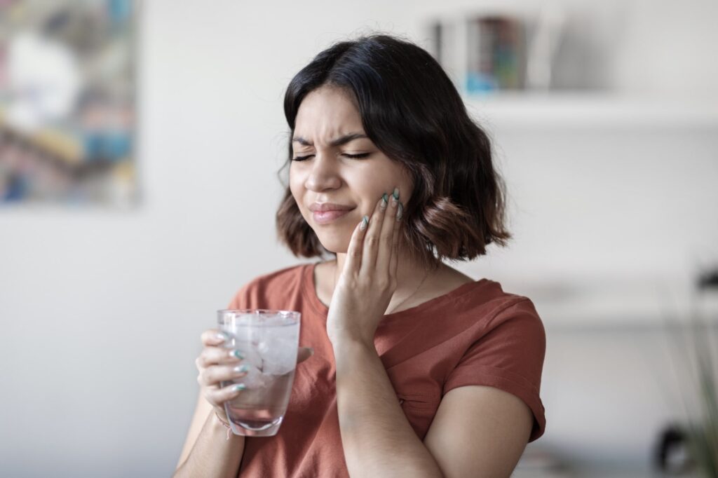 Young woman drinking water with ice and touching her cheek