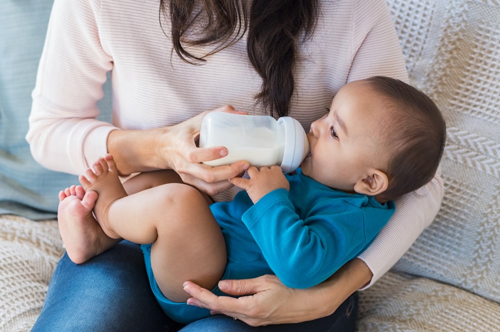 Little infant baby lying on mothers hand drinking milk from bottle