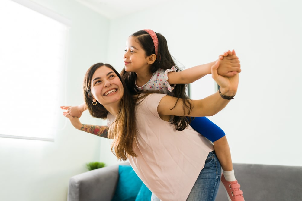 Playful happy mom giving a piggyback to her little happy daughter