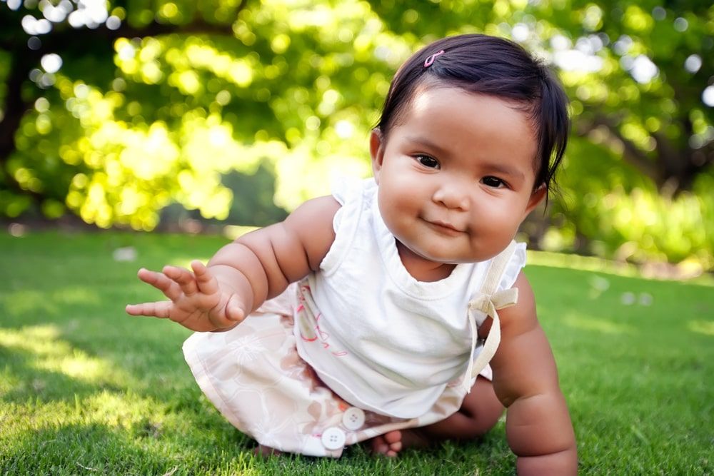 Cute baby girl with a smile on her face, reaching out to take her first crawling step