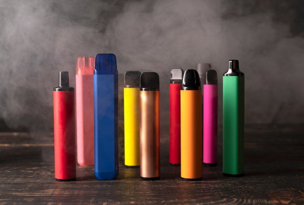 Set of colorful disposable electronic cigarettes on a dark wood background with smoke