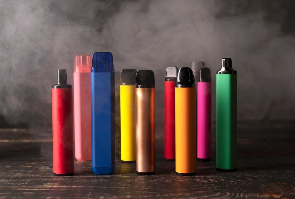 Set of colorful disposable electronic cigarettes on a dark wood background with smoke