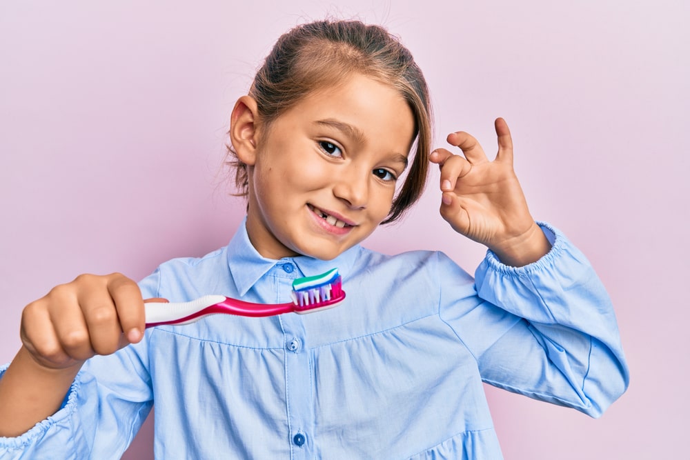 Little beautiful girl holding toothbrush with toothpaste doing