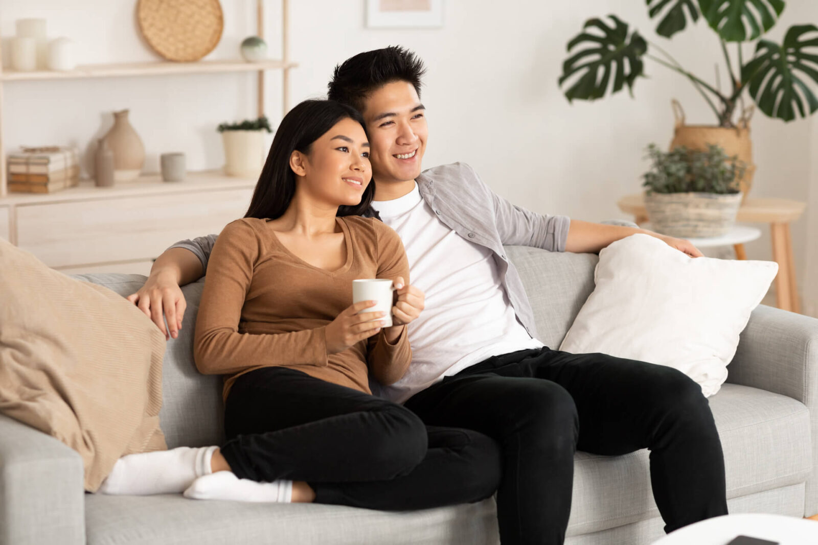 Lovely filipino couple watching film resting on a couch at home, copy space