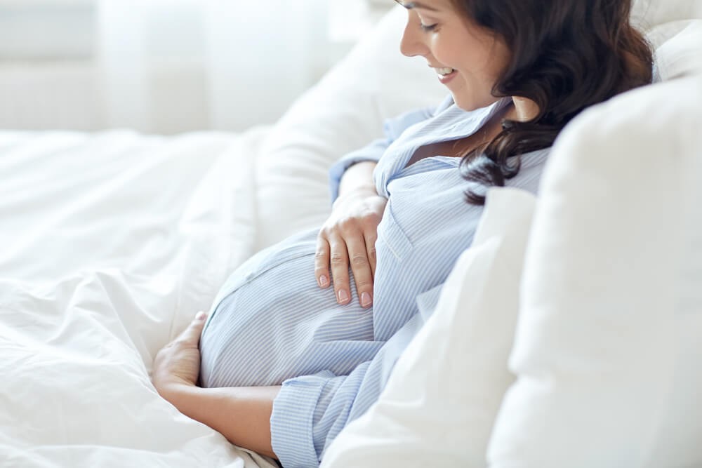 happy smiling pregnant woman lying in bed and touching her belly at home