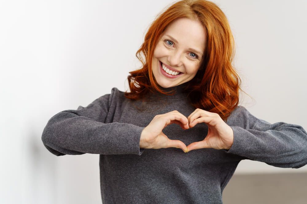 young redhead woman making a heart gesture with her fingers