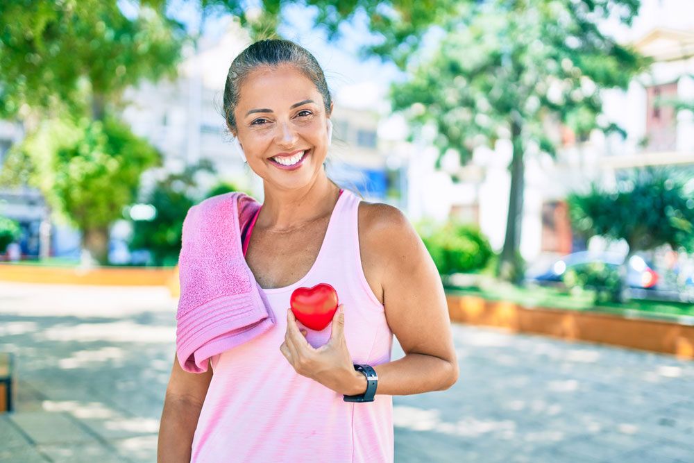 Middle age sportswoman holding heart at the park