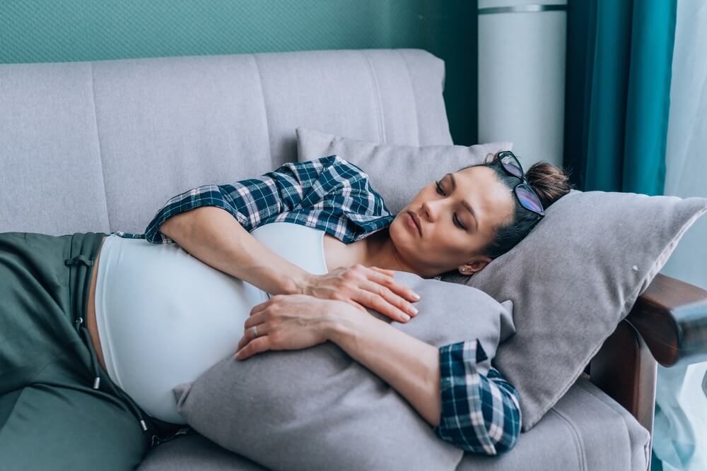 Young sad lonely pregnant woman lying on sofa at home