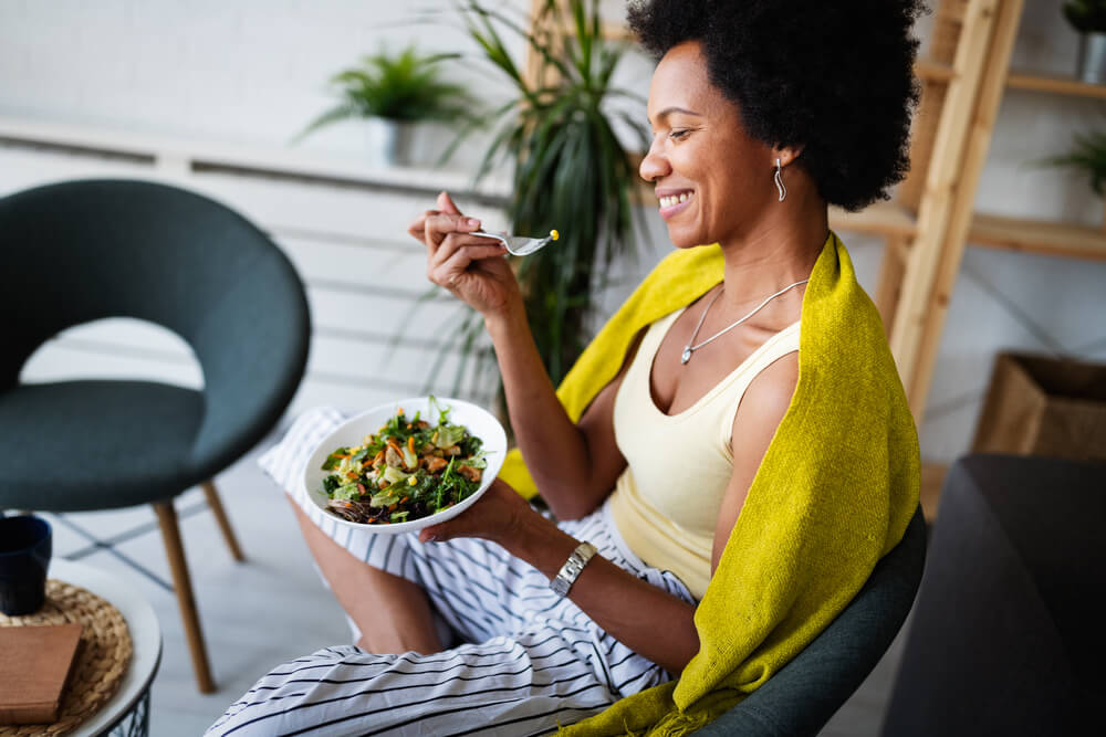 Beautiful afro american woman eating vegetable salad at home.