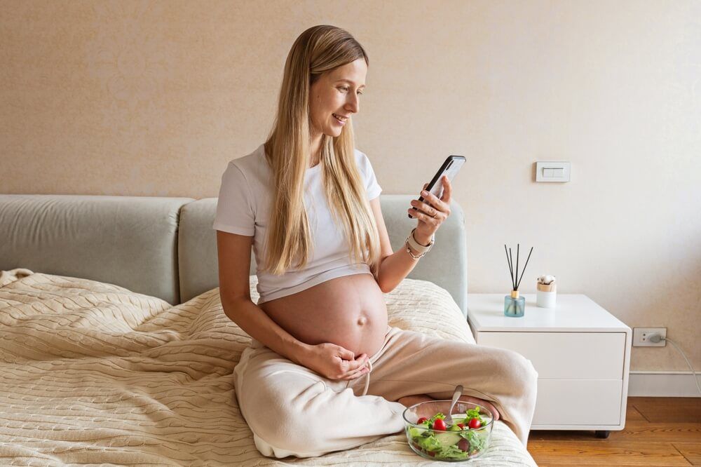 Happy young pregnant woman using mobile phone at home