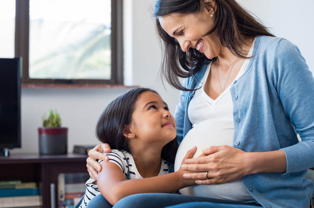 Lovely daughter touching mother's pregnant belly.