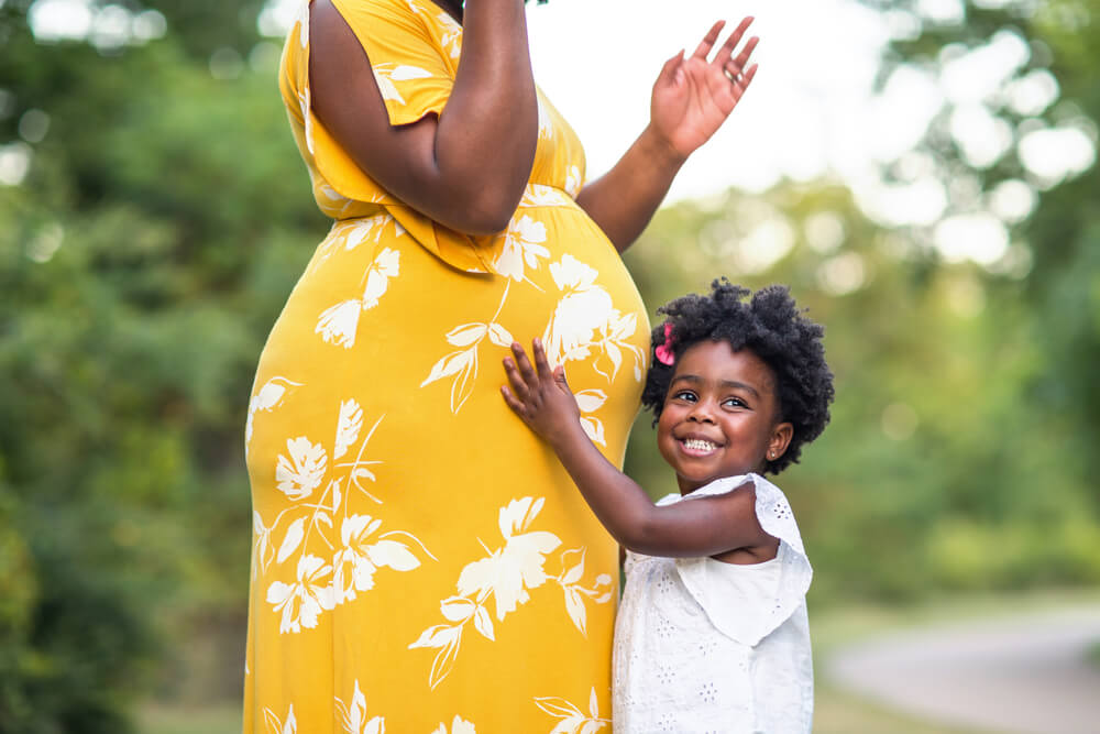 Little girl smiling holding her mother’s stomach