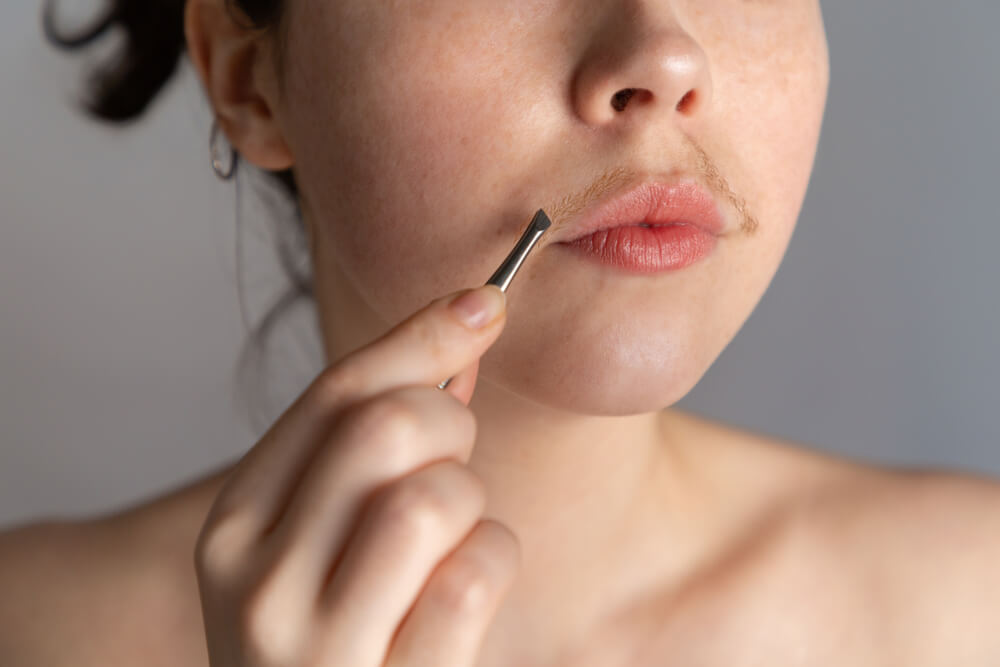 A young woman with a mustache tries to remove the hair over her lip