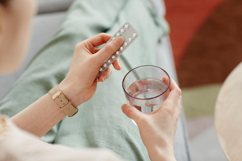 young woman taking birth control pills with glass of water,