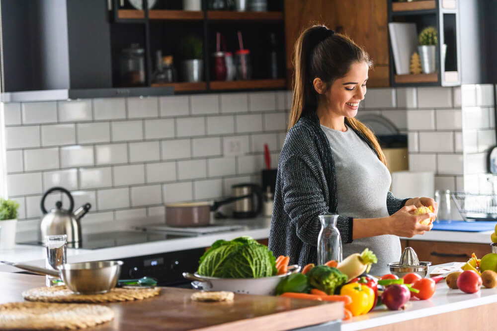 Beautiful smiling young pregnant woman preparing healthy food