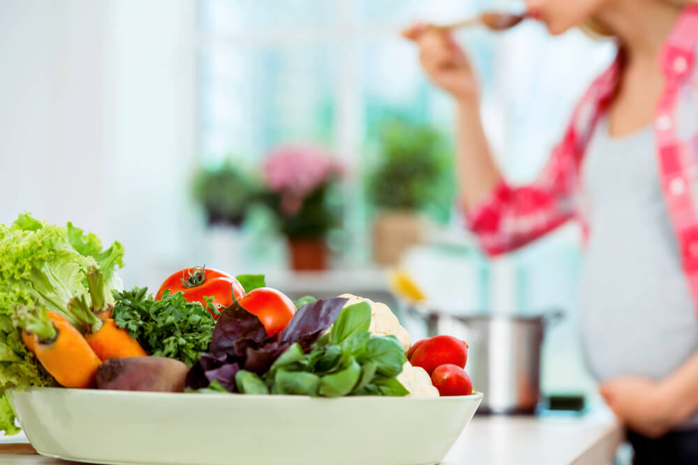 Young blonde pregnant woman cooking in kitchen.