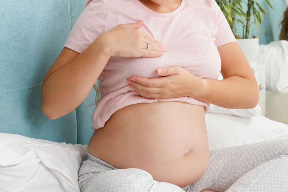 Young pregnant woman with big belly checking and touching her breast before lactation