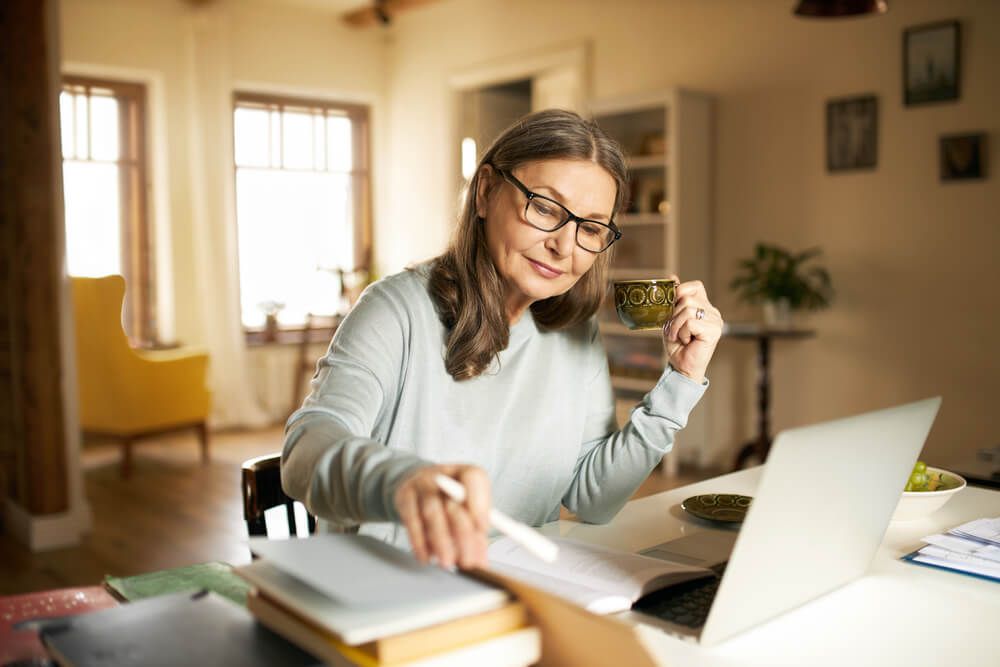 Serious confident middle aged female with cup of coffee sitting at desk