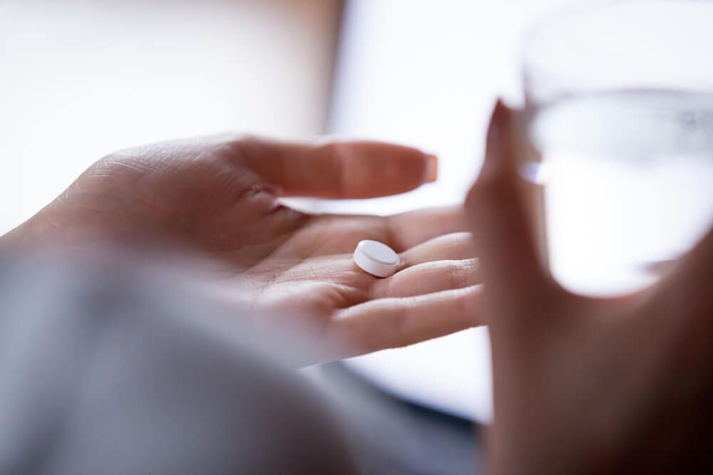 woman holding pill in hand with water.