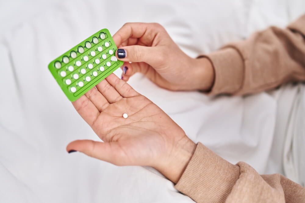 Young hispanic woman holding birth control pills at bedroom