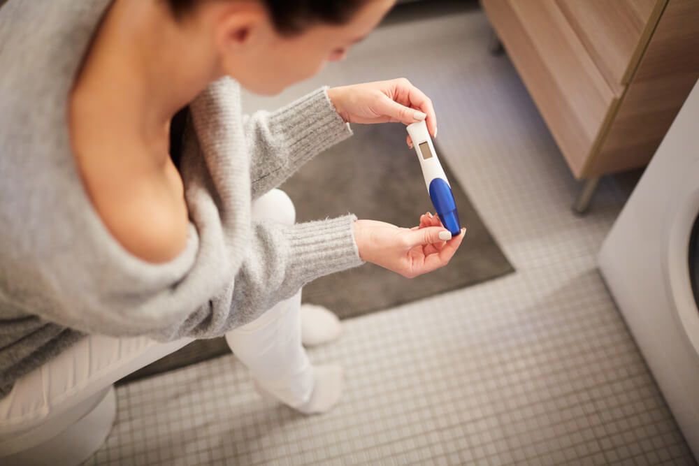 young woman sitting in bathroom and checking result of pregnancy test