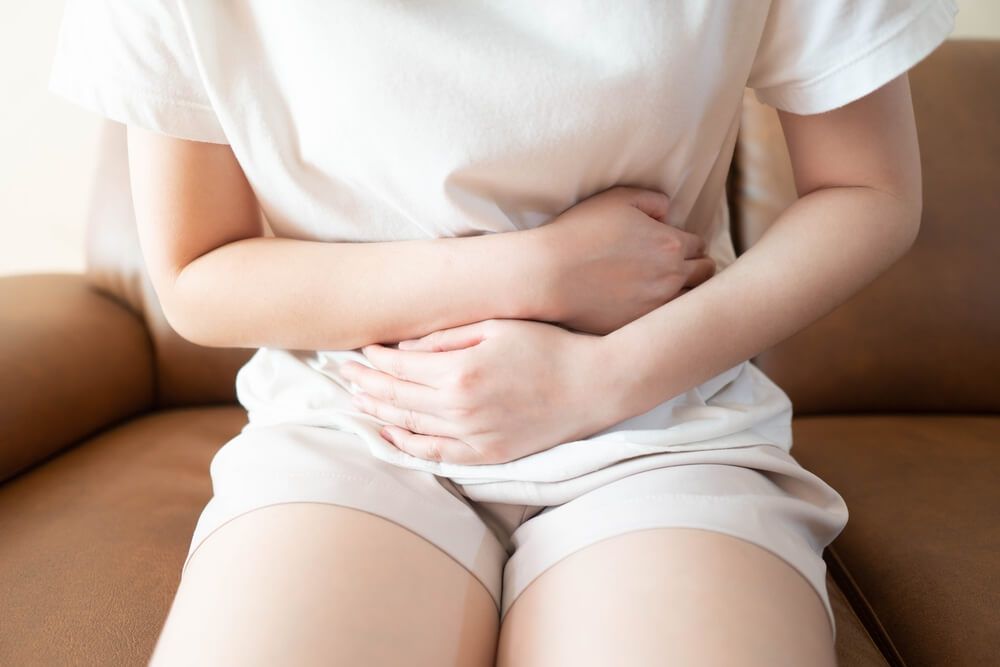 Young female suffering form stomach ache while sitting on couch at home