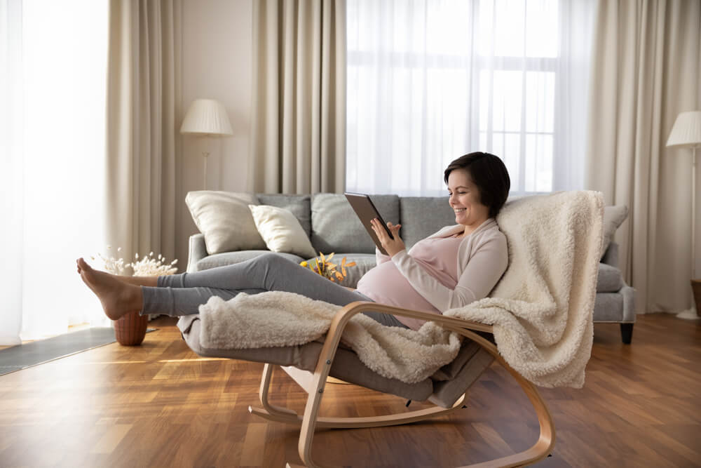 pregnant relax in armchair in cozy living room look at tablet screen