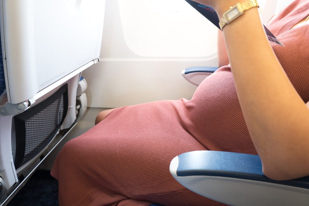 Happy pregnant woman is traveling to destination by plane sitting and reading book