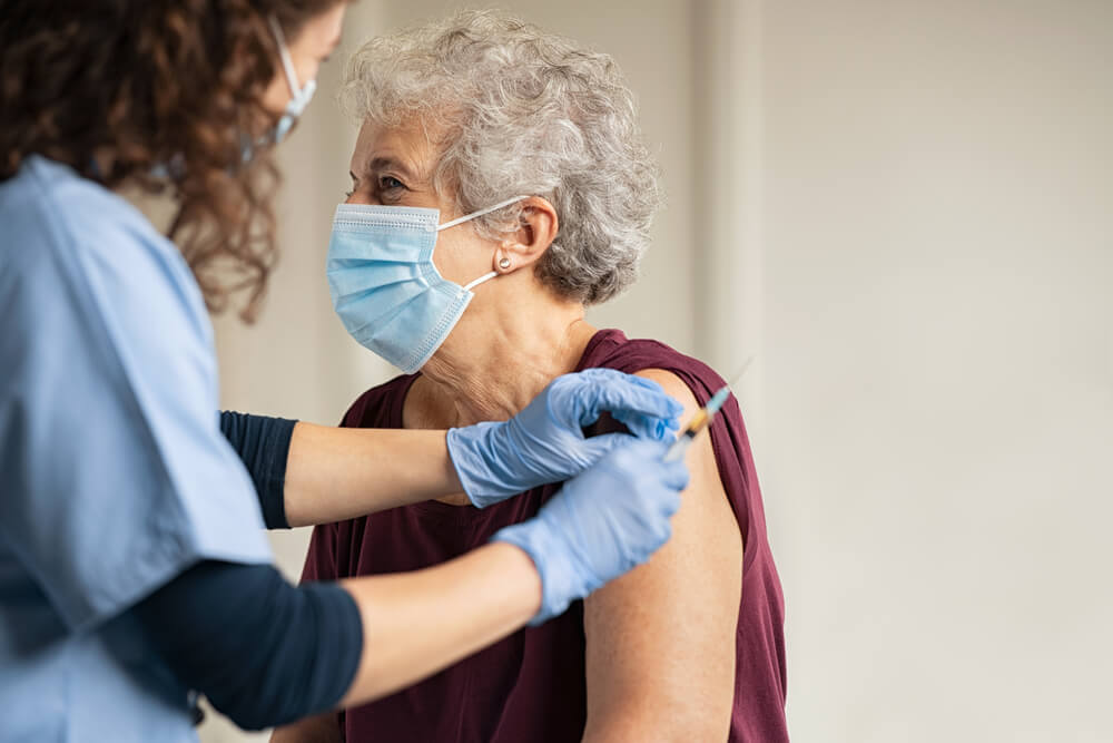 General practitioner vaccinating old patient in clinic