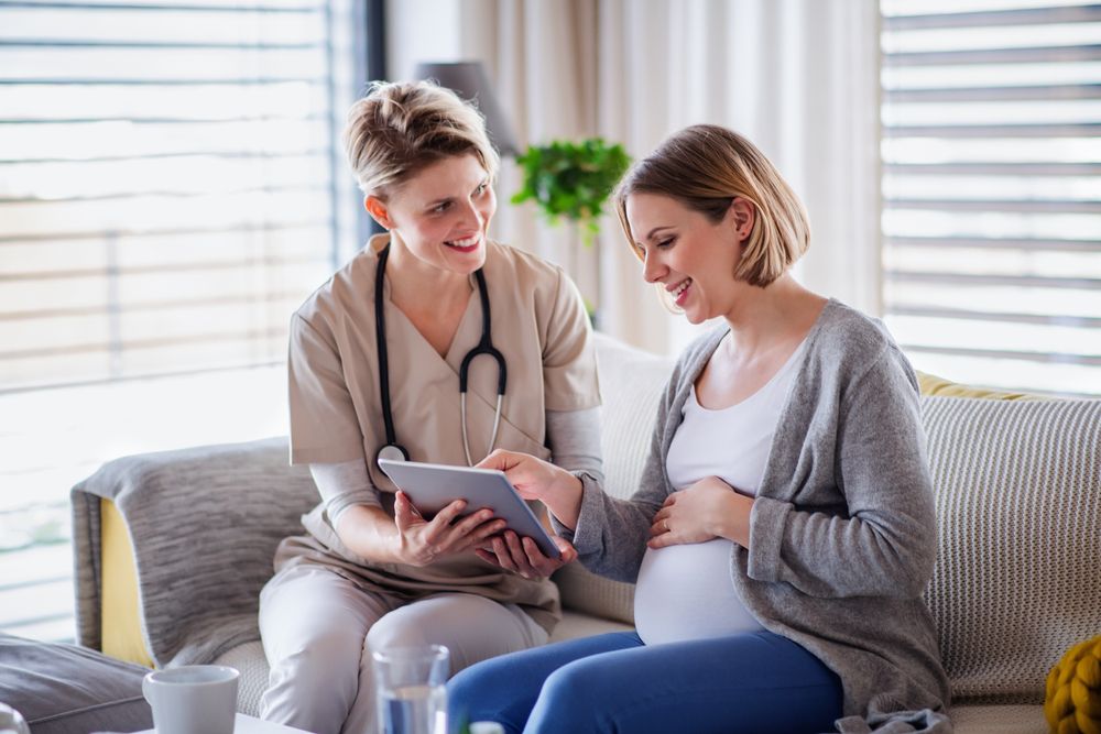 A healthcare worker with tablet talking to pregnant woman at home.