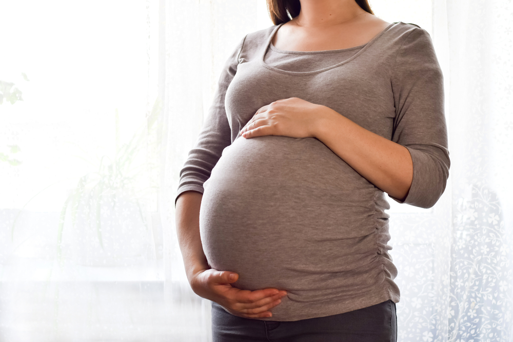 Young pregnant woman holds her hands on her swollen belly.