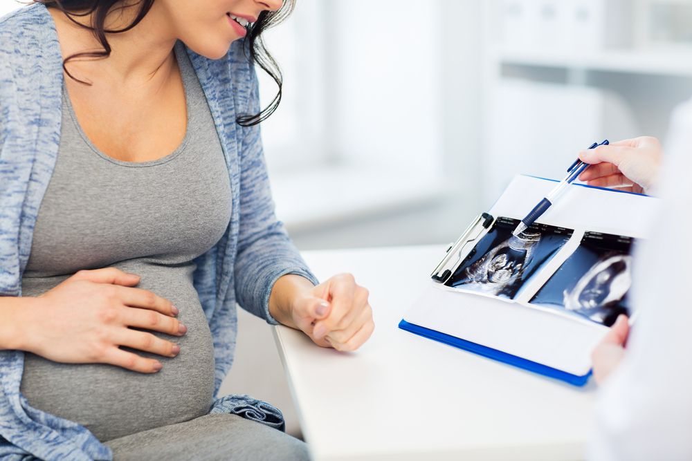 Second Trimester Screening Tests, Pregnancy, gynecology, medicine, health care and people concept - close up of gynecologist doctor showing ultrasound image on clipboard to pregnant woman at hospital
