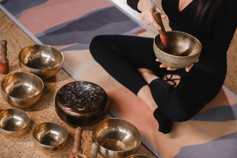 Close-up of a woman's hands sitting in a lotus position using a singing bowl indoors. Relaxation and meditation