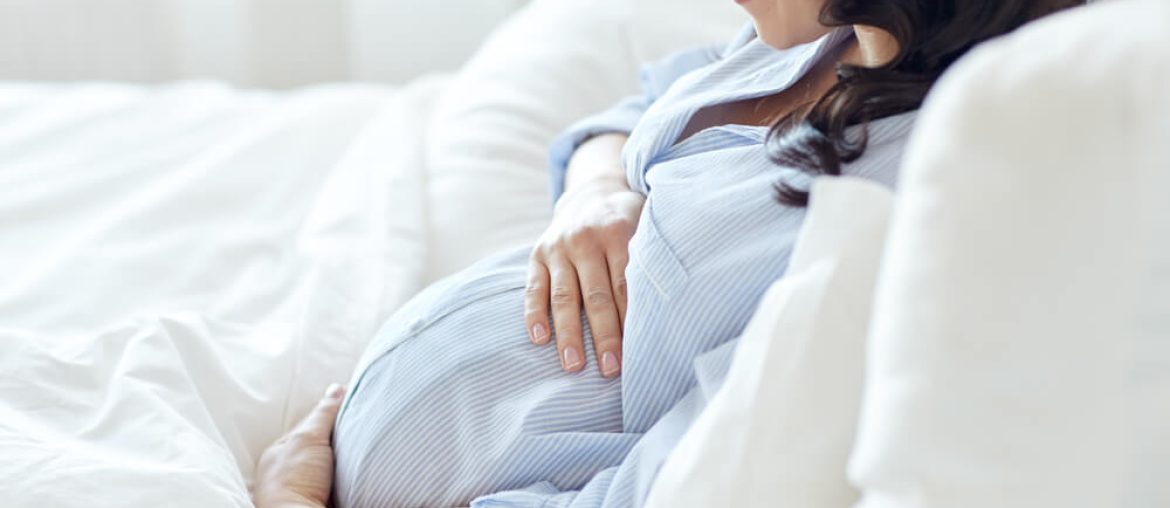 happy smiling pregnant woman lying in bed and touching her belly at home