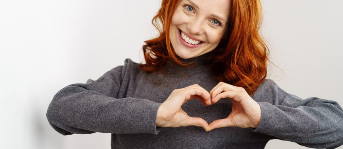 young redhead woman making a heart gesture with her fingers
