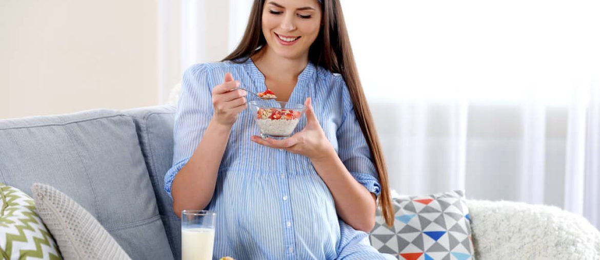 Young pregnant woman with milk and breakfast on sofa