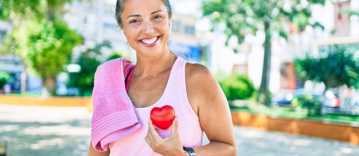 Middle age sportswoman holding heart at the park