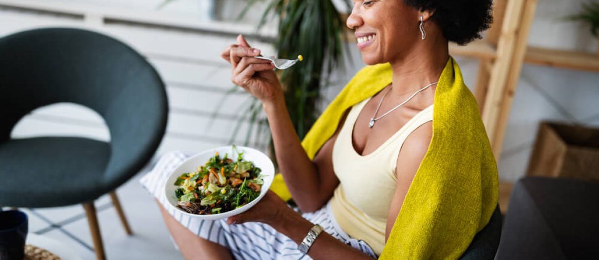 Beautiful afro american woman eating vegetable salad at home.