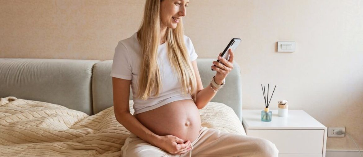 Happy young pregnant woman using mobile phone at home