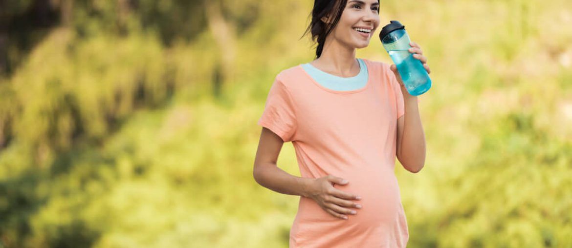 A woman in a pink T-shirt is walking in the park with a sports bottle in her hands
