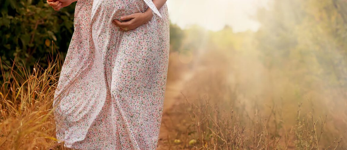 Stomach of the pregnant woman in a summer dress on the road outdoors