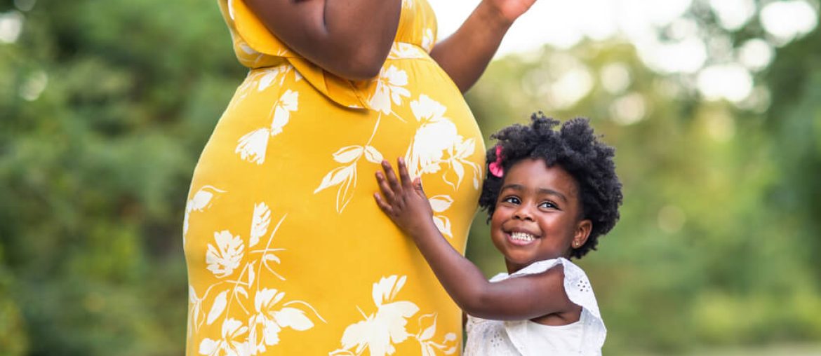 Little girl smiling holding her mother’s stomach