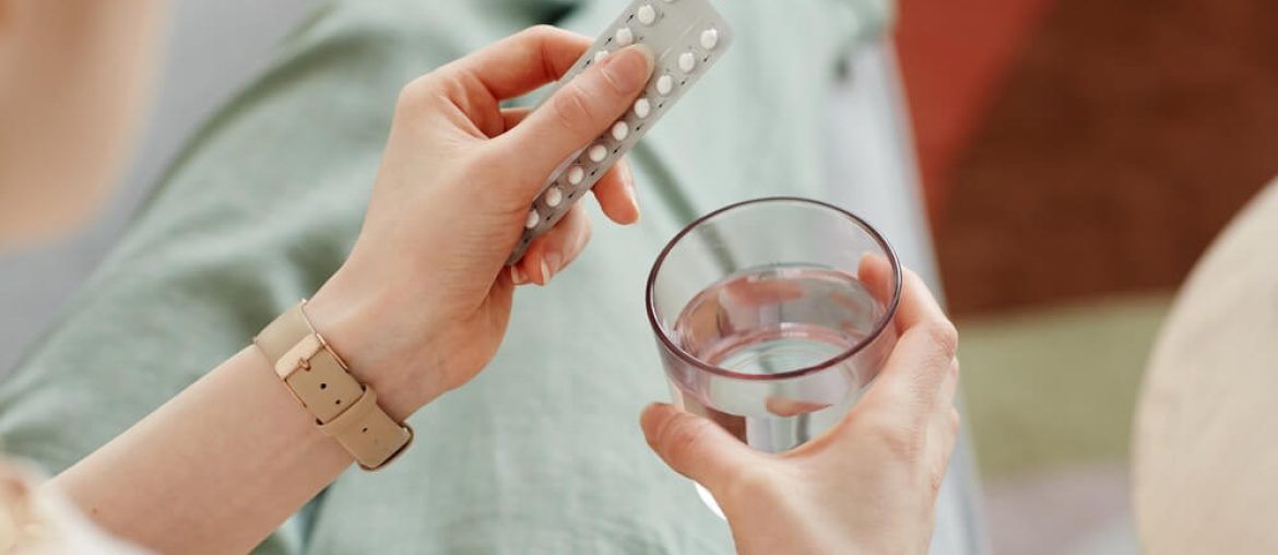 young woman taking birth control pills with glass of water,