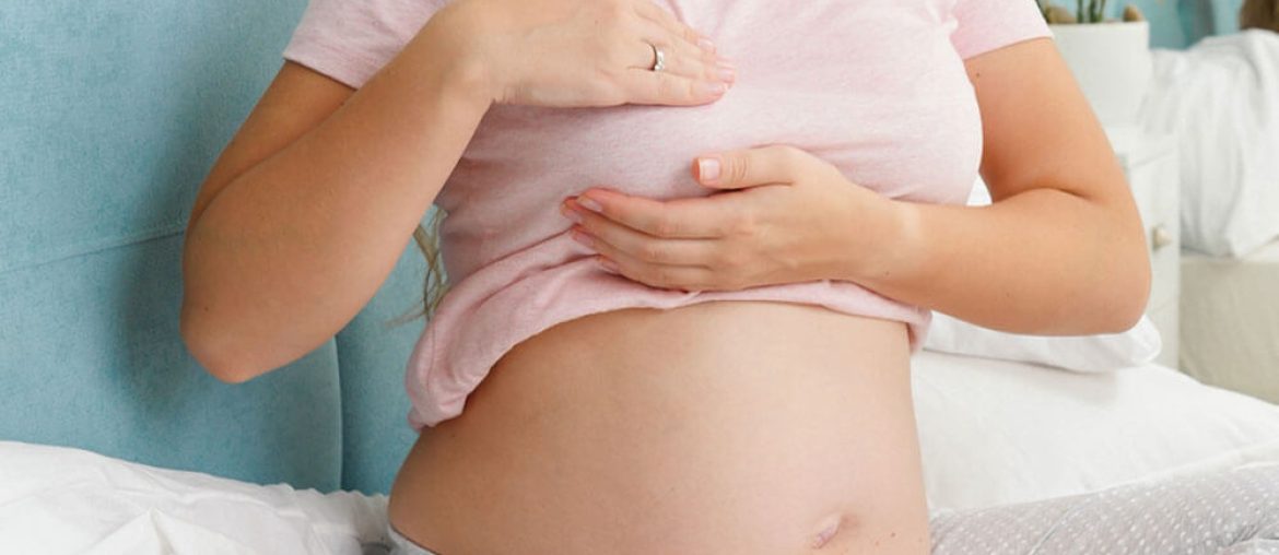 Young pregnant woman with big belly checking and touching her breast before lactation