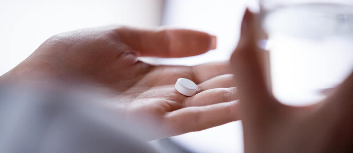 woman holding pill in hand with water.