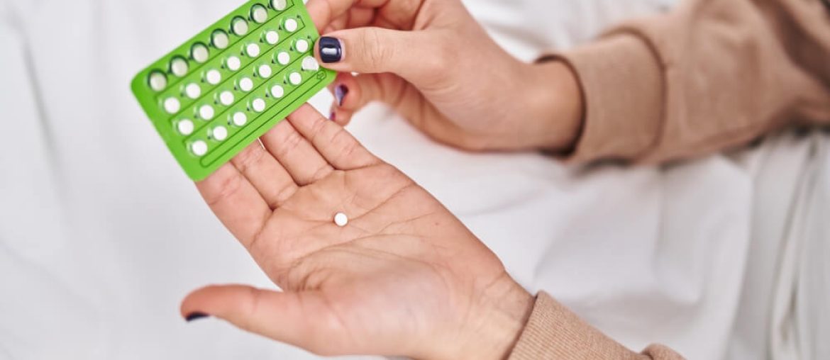 Young hispanic woman holding birth control pills at bedroom