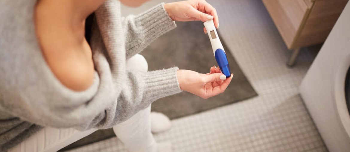 young woman sitting in bathroom and checking result of pregnancy test